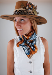 Woman wearing a decorative hat and printed scarf against a plain background
