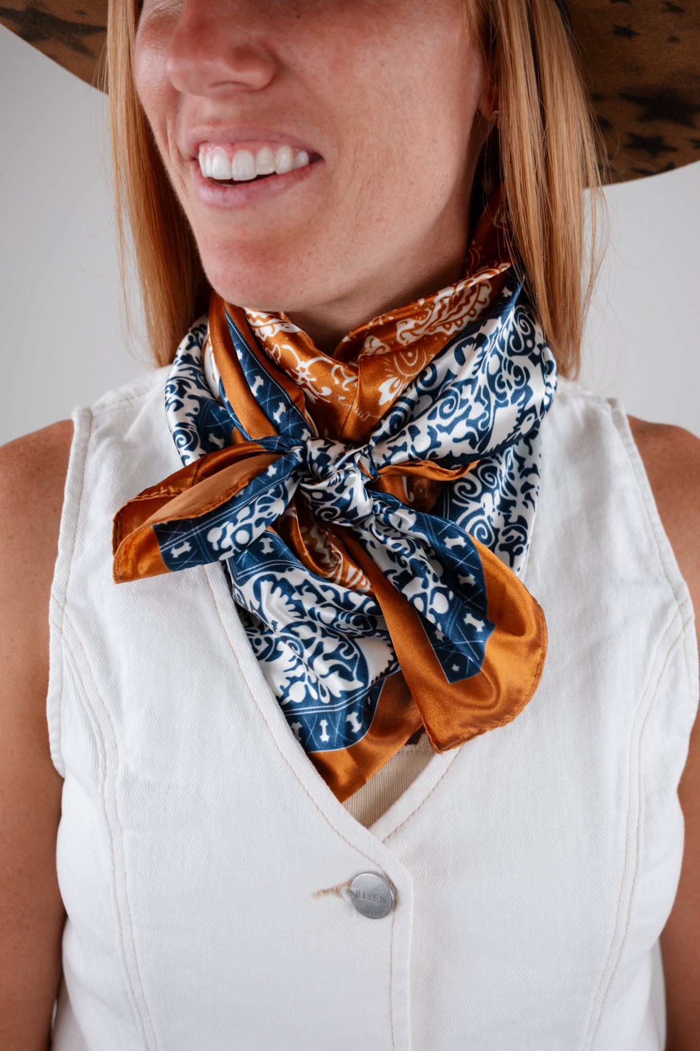 Woman wearing a white sleeveless top with a patterned scarf around her neck.