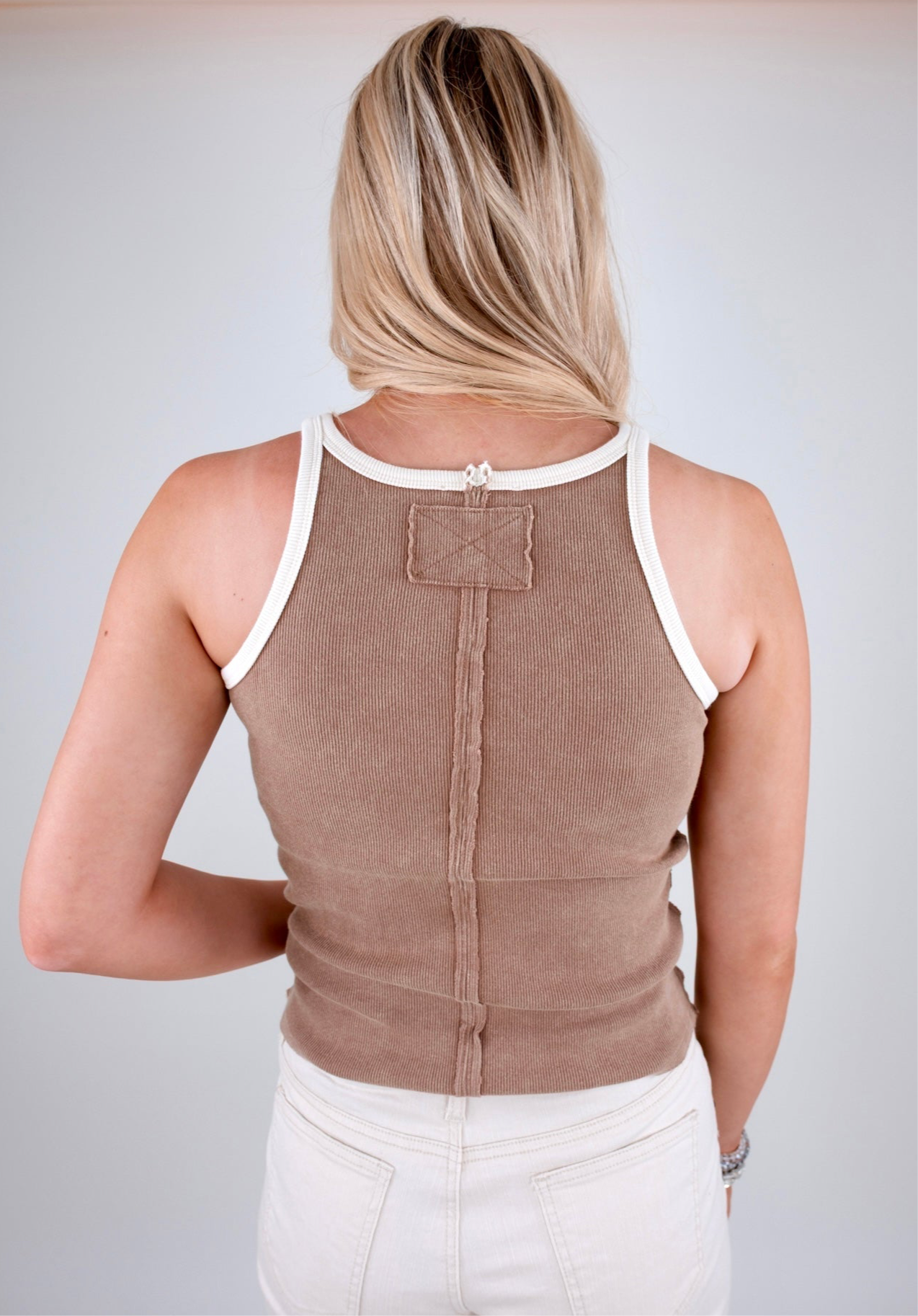 Person wearing a brown tank top with white trim on a plain background