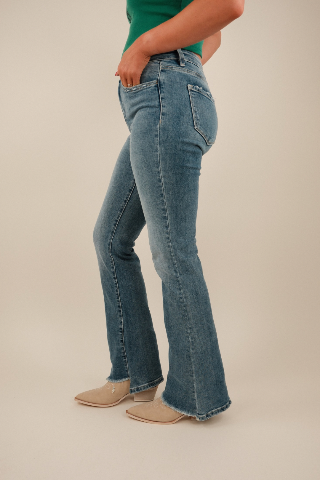 Angled side shot highlighting slanted hem detail, high‑rise fit, western flare silhouette and stretchy medium‑wash jean fabric.