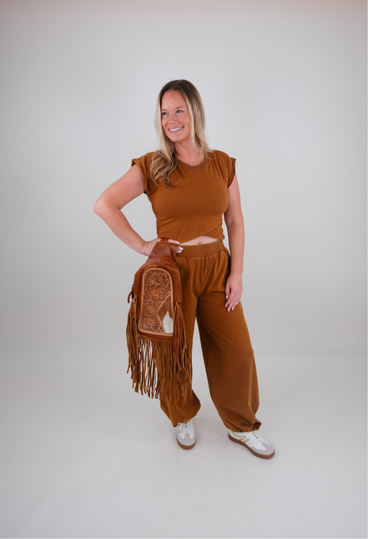 Woman in brown outfit set holding a fringed bag on a white background