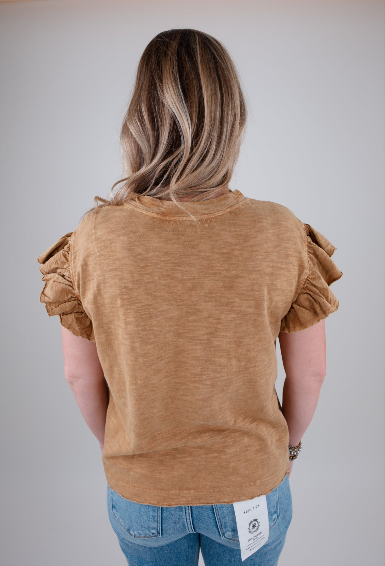 Person wearing a camel colored top with ruffled sleeves on a plain background