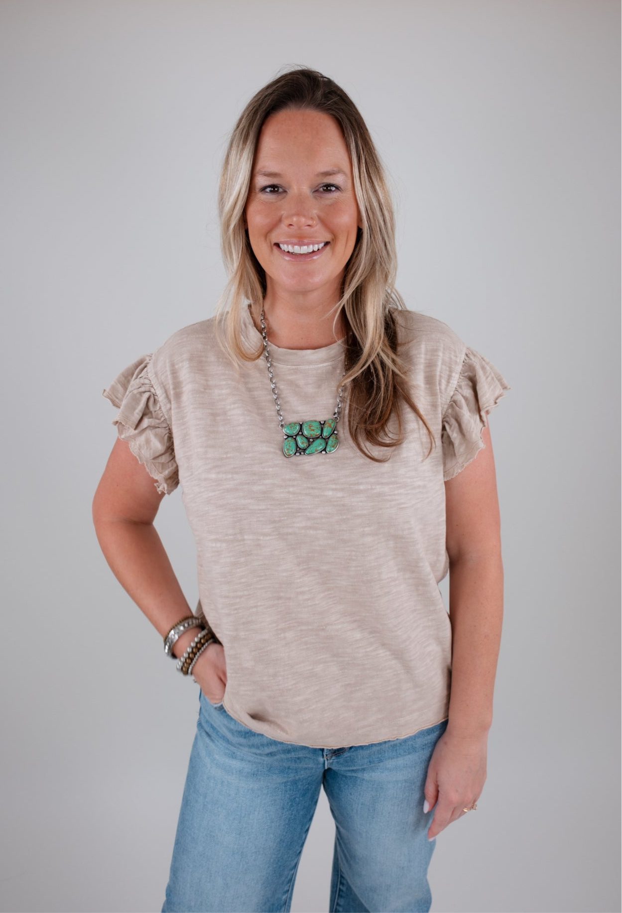 Woman wearing a beige ruffled sleeve top and blue jeans against a plain background
