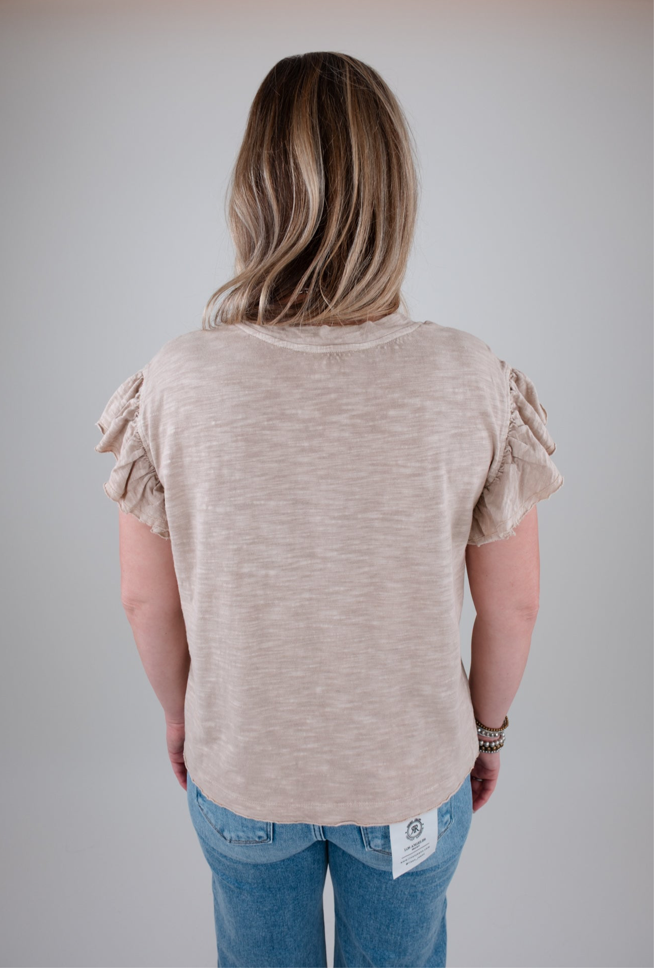 Person wearing a beige ruffled sleeve top and blue jeans on a plain background