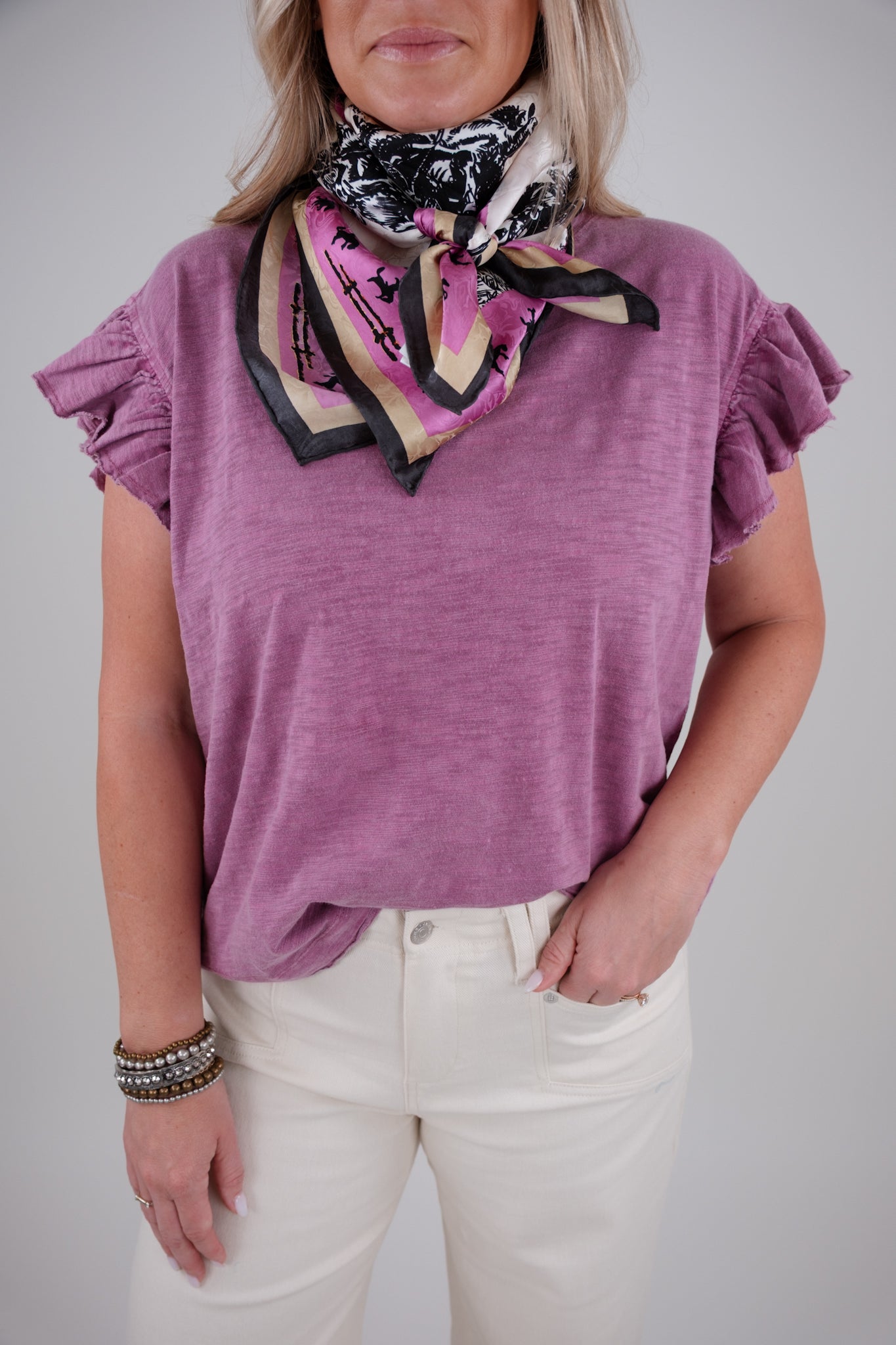 Person wearing a purple top and white pants with a colorful scarf around their neck against a gray background