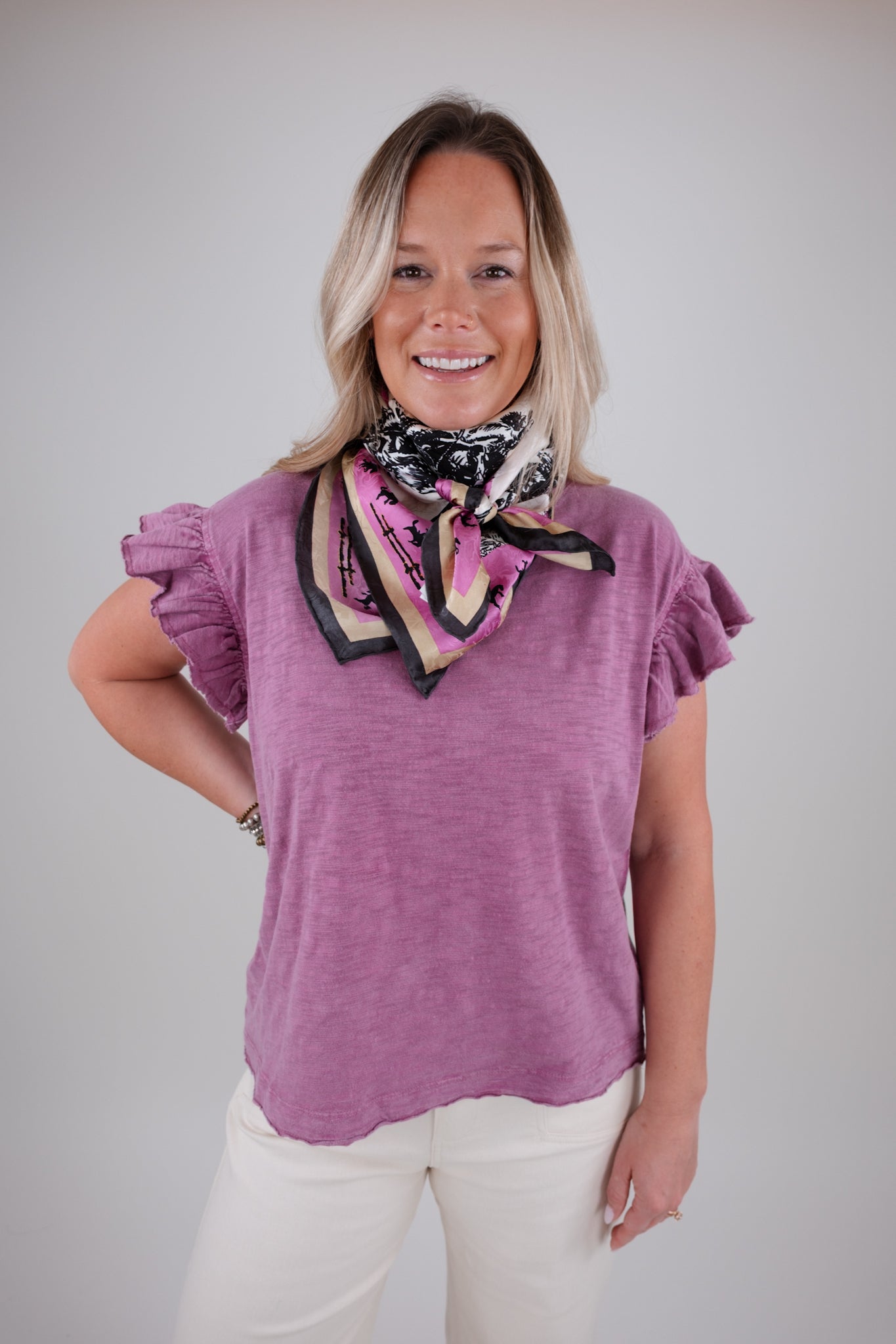 Woman wearing a purple ruffle sleeved top and colorful scarf against a plain background