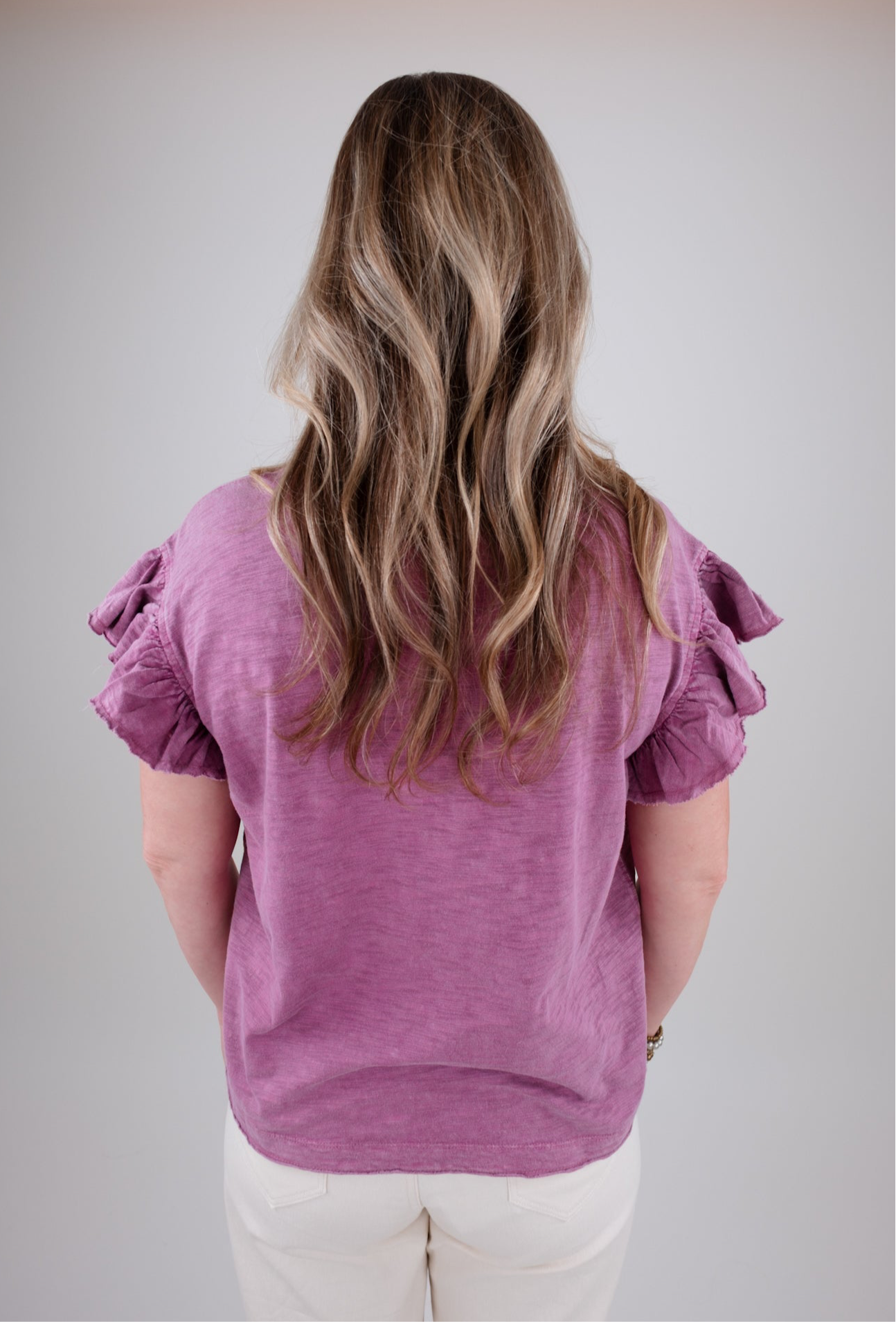 Person wearing a purple top with ruffled sleeves on a plain background