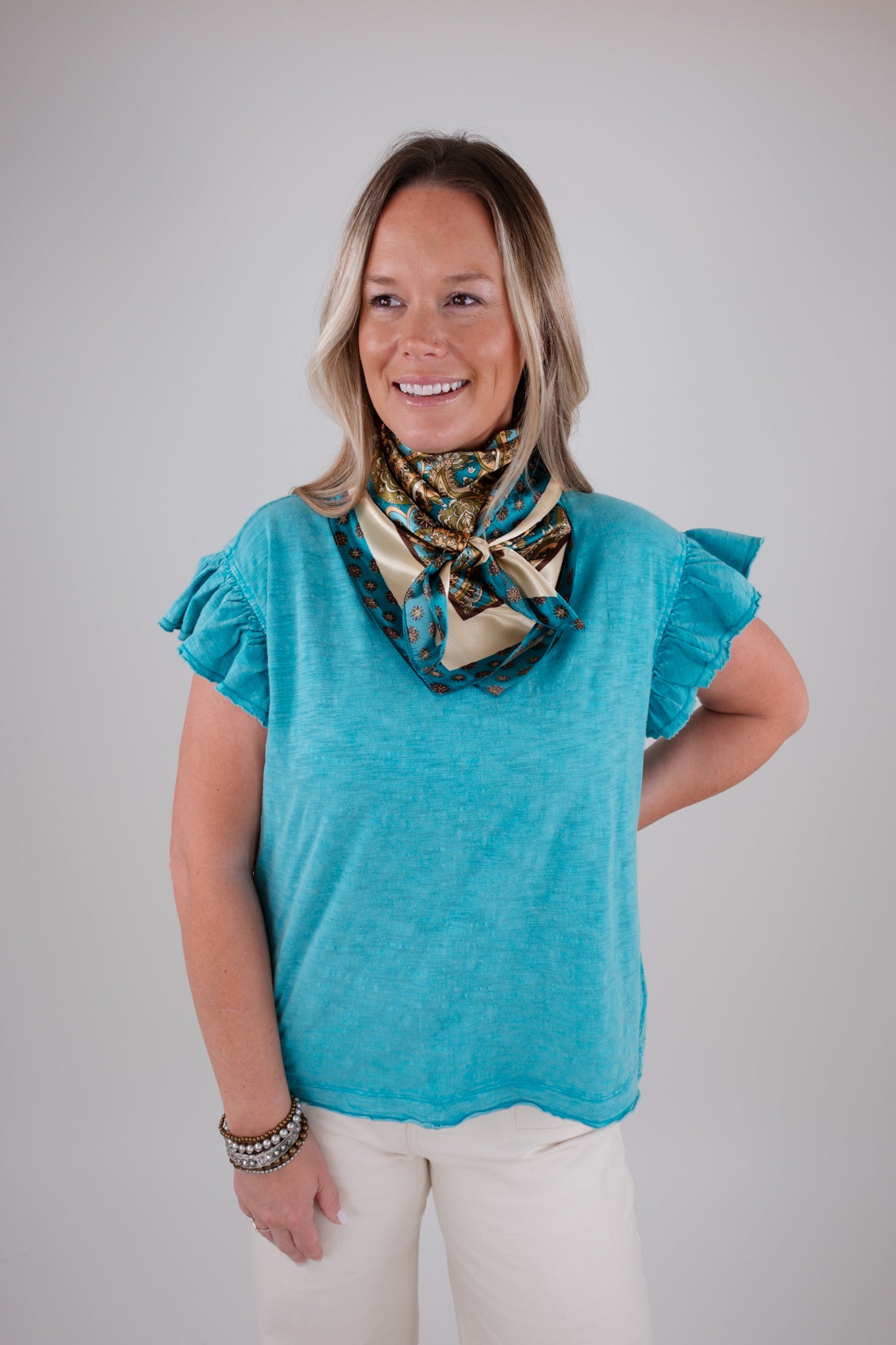 Woman wearing a blue top with ruffled sleeves and patterned scarf on a plain background