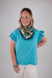 Woman wearing a blue top with ruffled sleeves and patterned scarf on a plain background