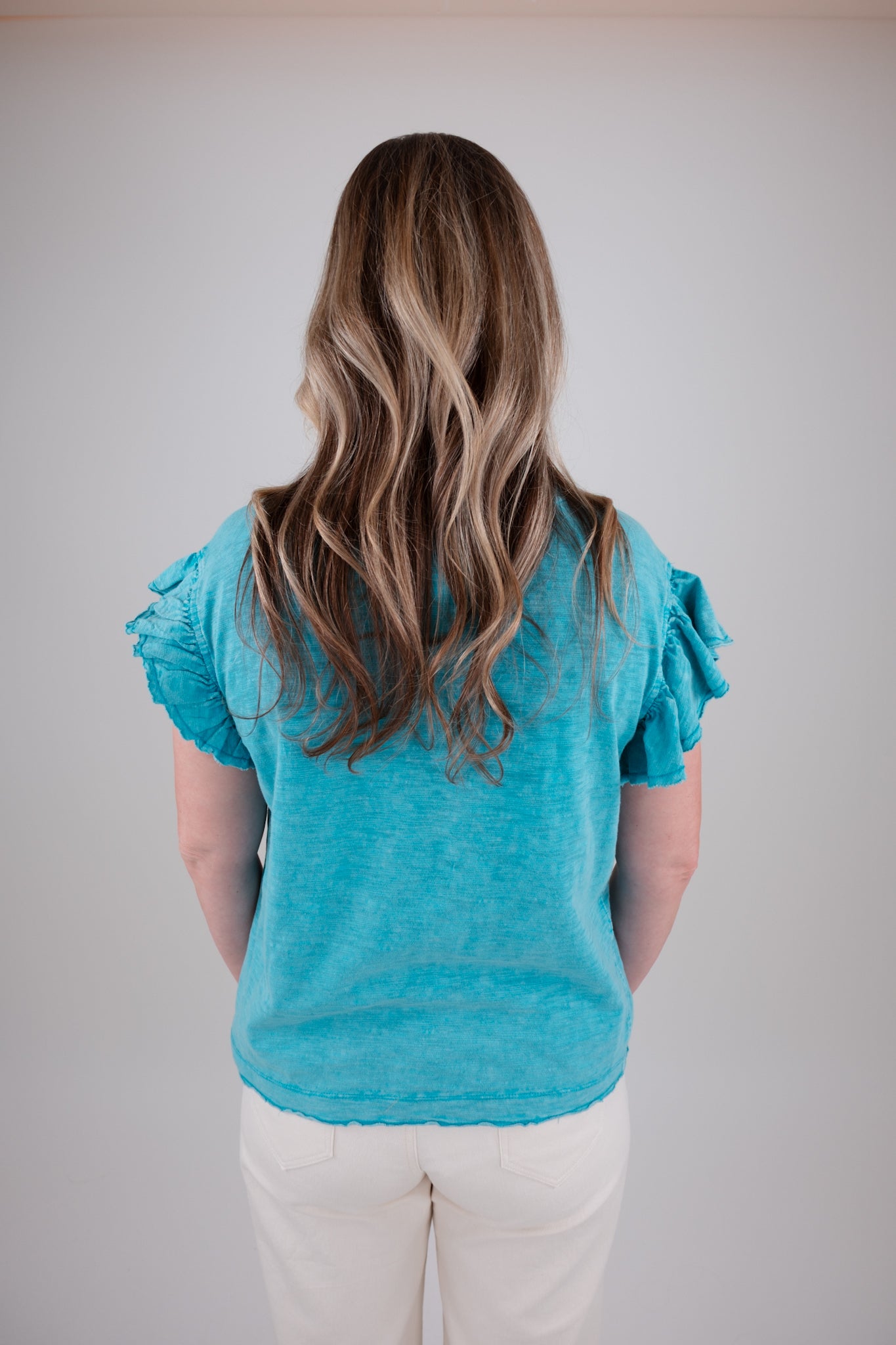 Person wearing a blue top with ruffled sleeves against a plain background