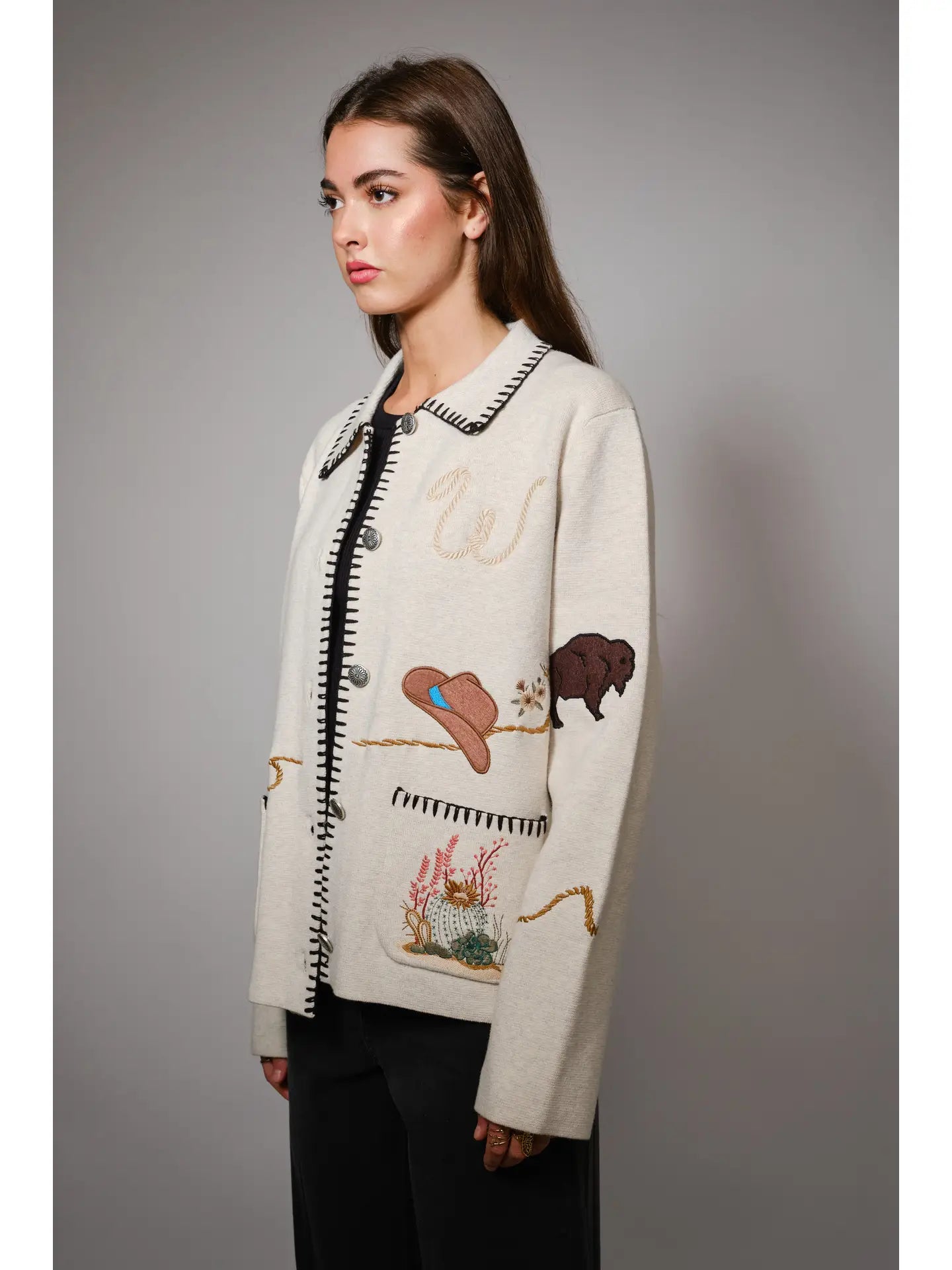 Woman wearing a cream-colored jacket with embroidered designs on a gray background