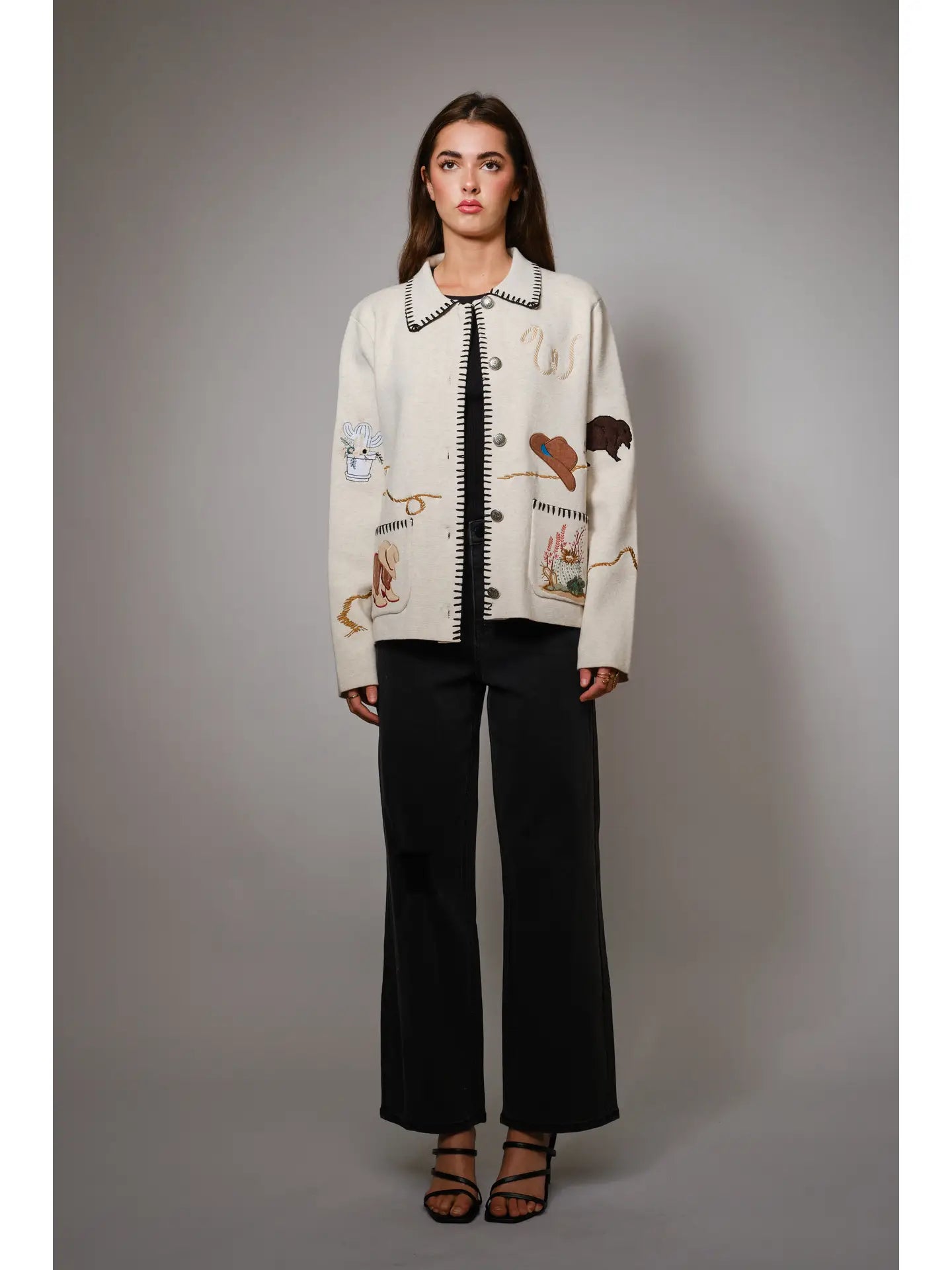 Woman wearing a cream jacket with animal-themed patches on a gray background