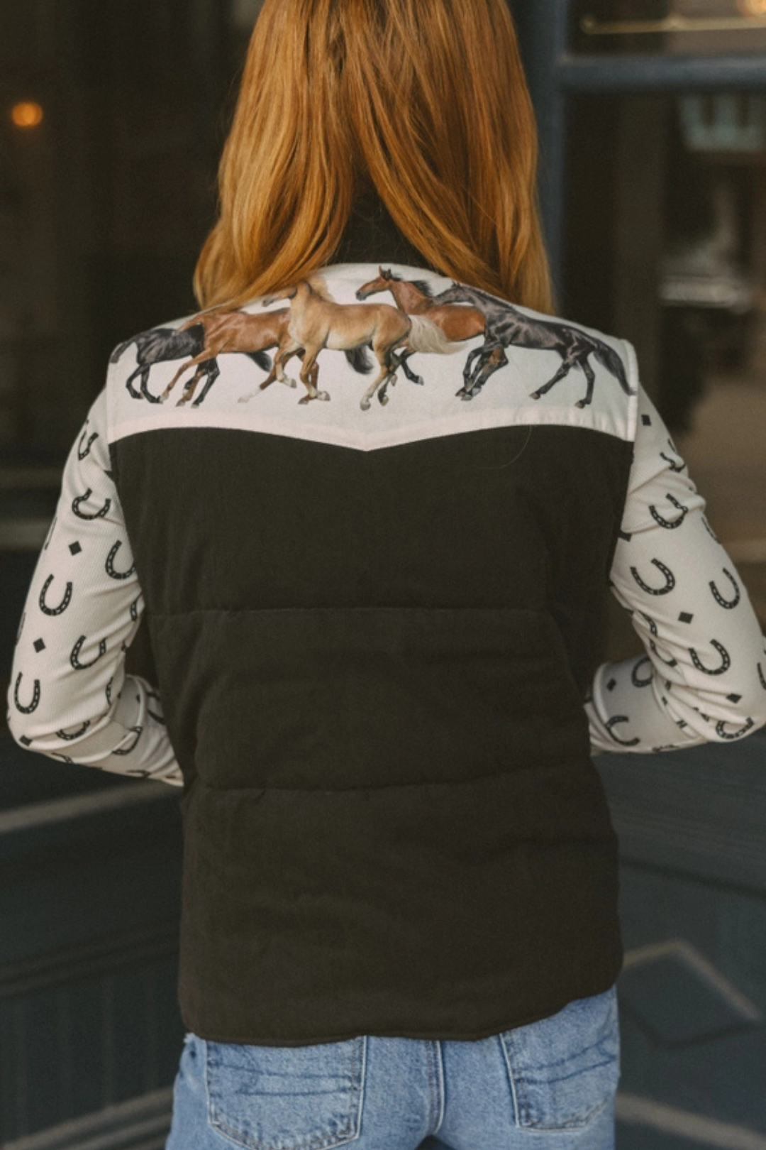 Person showing the back of a black vest over a patterned shirt with horse designs.