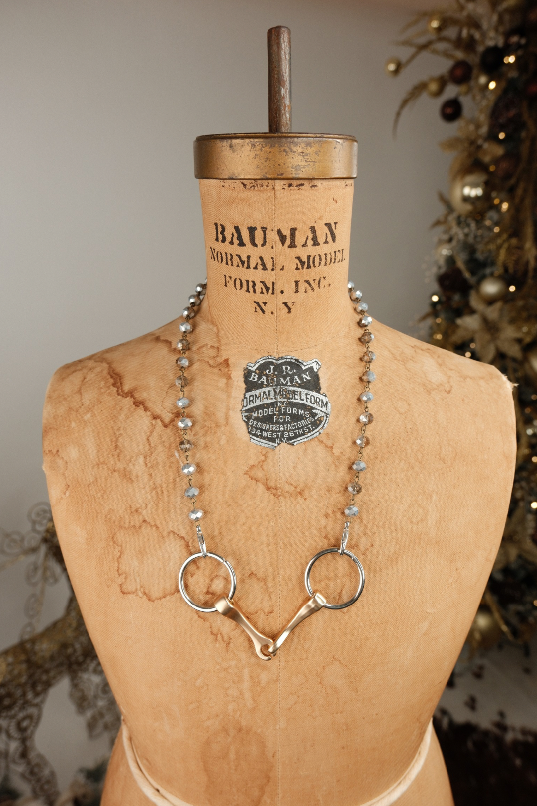 Bit necklace on a mannequin with 'Bauman' label, decorative background