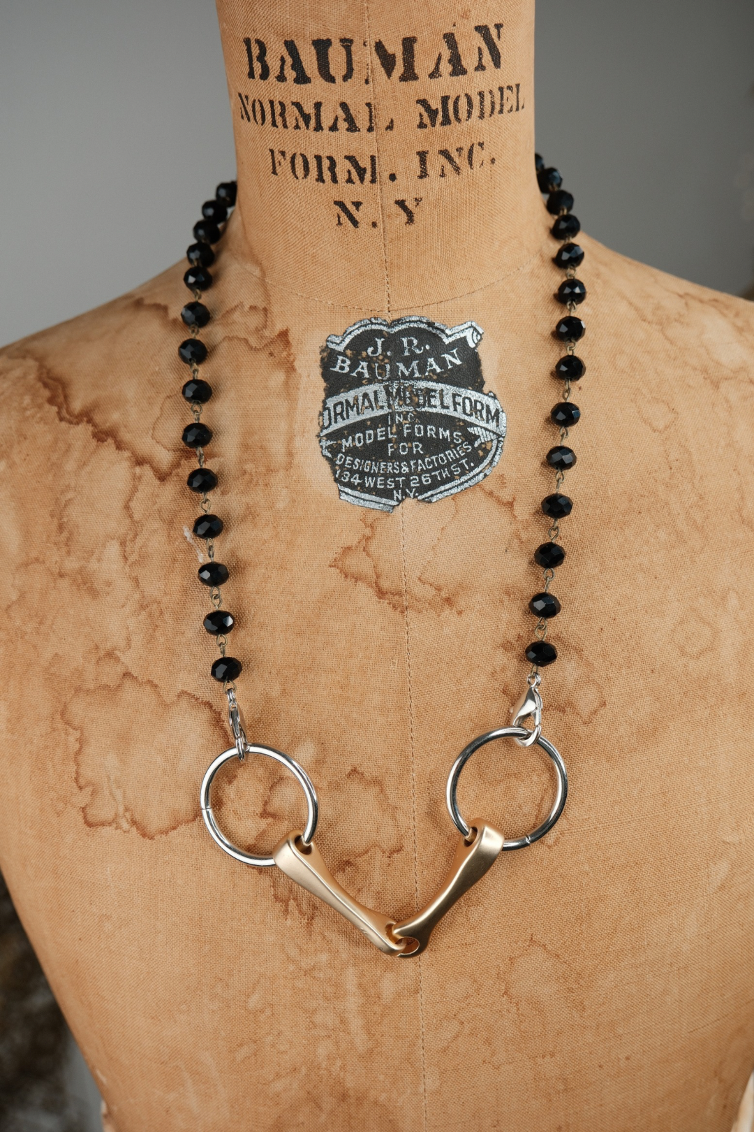 Necklace with horse bit pendant on a mannequin bust with 'Bauman Normal Model Form Inc.' label.