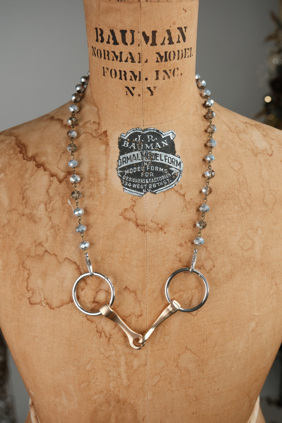 Mannequin wearing a necklace with a horse bit pendant and a Bauman Normal Model Form Inc. badge.