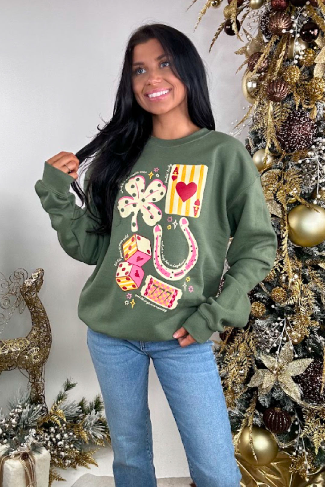 Woman wearing a green sweatshirt with colorful designs in front of a decorated Christmas tree.