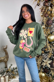 Woman wearing a green sweatshirt with colorful designs in front of a decorated Christmas tree.