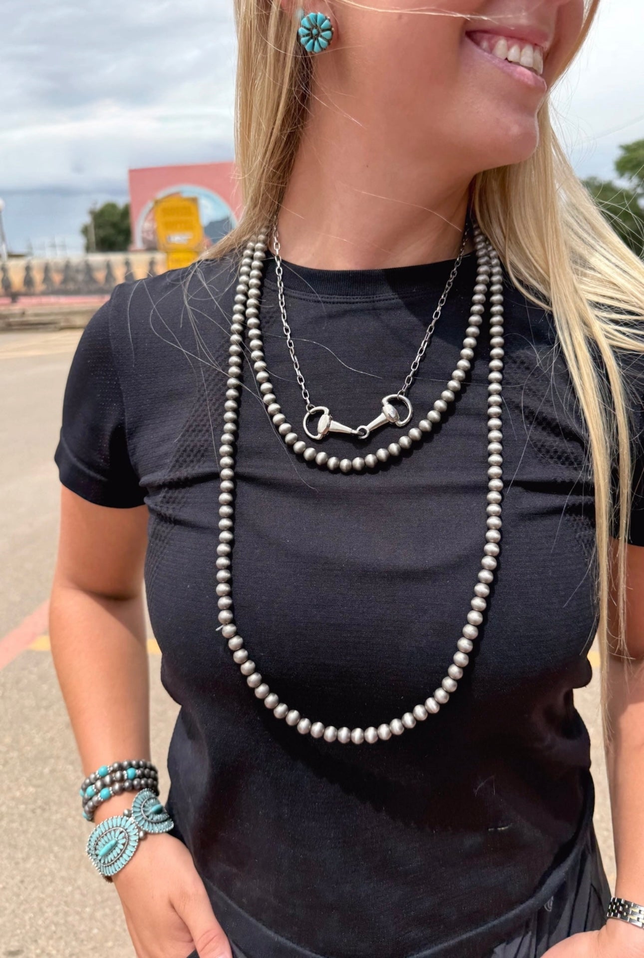 Woman wearing a black top with layered necklaces and accessories outdoors.