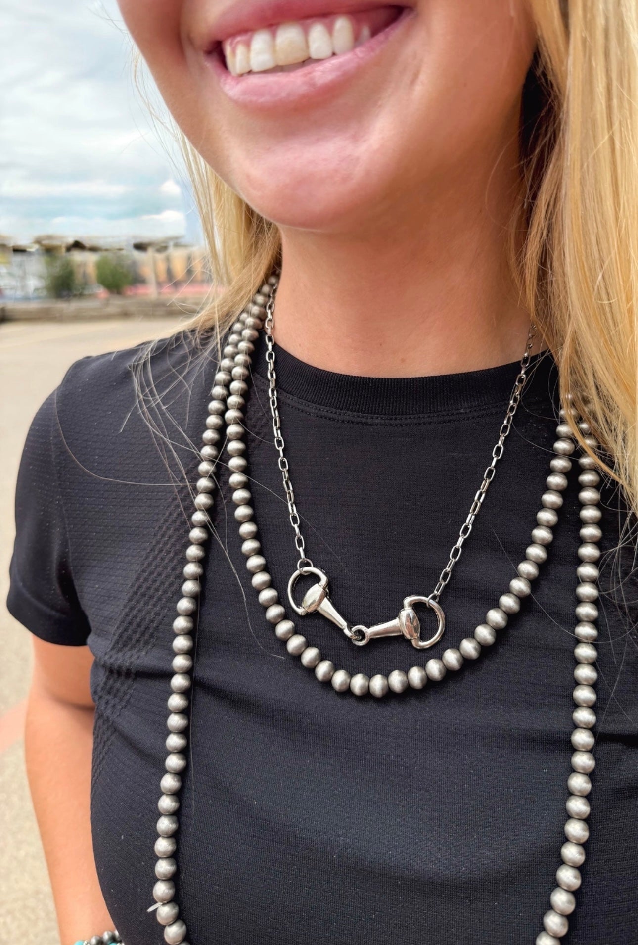 Woman wearing a black top and navajo pearl necklace with a silver horse bit pendant.