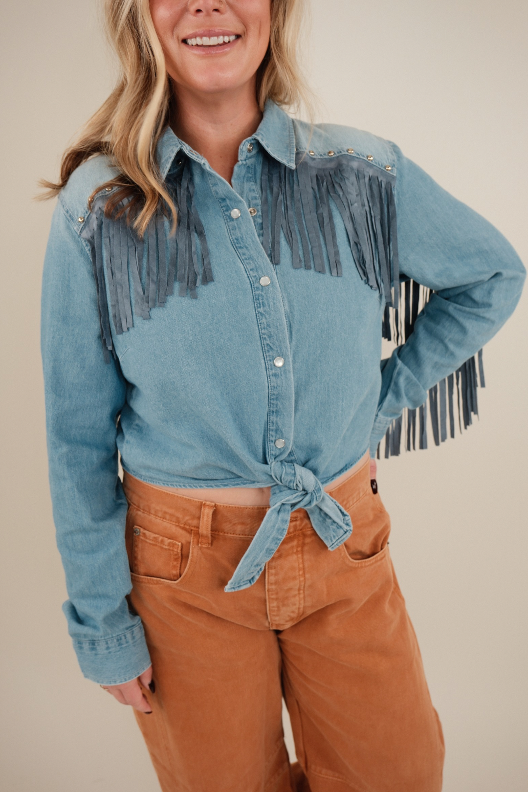 Close-up of High Noon Fringe Denim Top highlighting studded shoulders, long fringe detail and snap button western design.