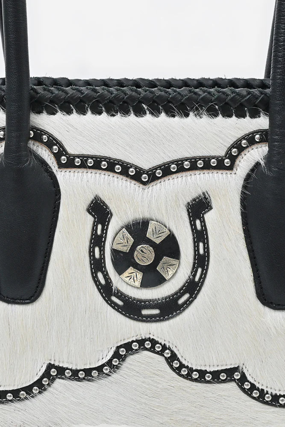 Close-up of a white hide handbag with black leather accents and decorative elements on a light gray background