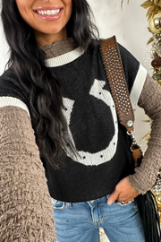 Woman wearing a black sweater with a horseshoe design, standing next to a decorated Christmas tree.
