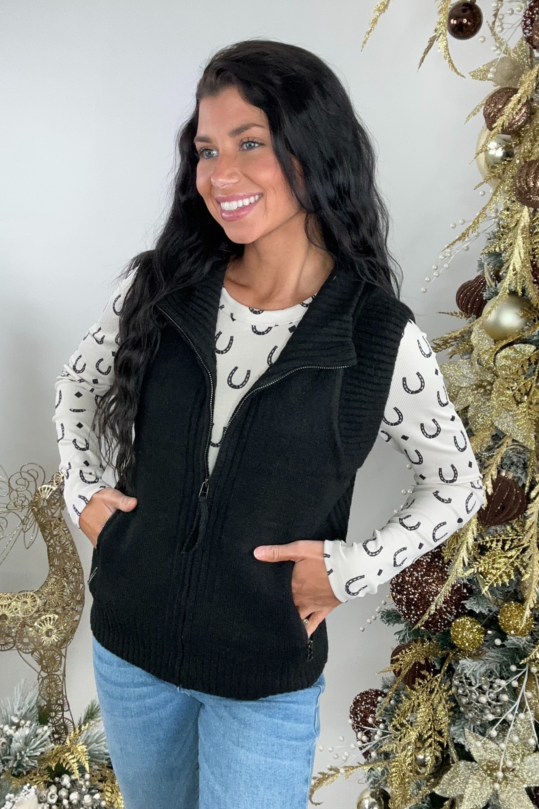Woman wearing a black vest over a horseshoe patterned shirt with a Christmas tree in the background