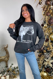 Woman wearing a dark gray sweatshirt with a horse graphic in front of a decorated Christmas tree.