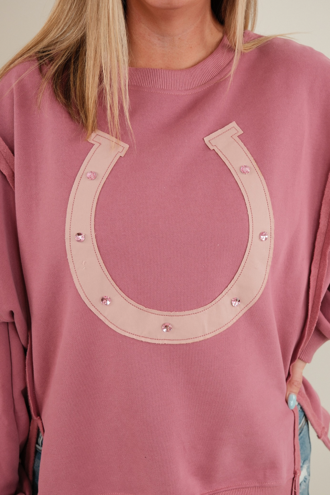 Close-up of Lucky Charm Pullover highlighting a cream horseshoe motif with shimmering pink gemstone embellishments.