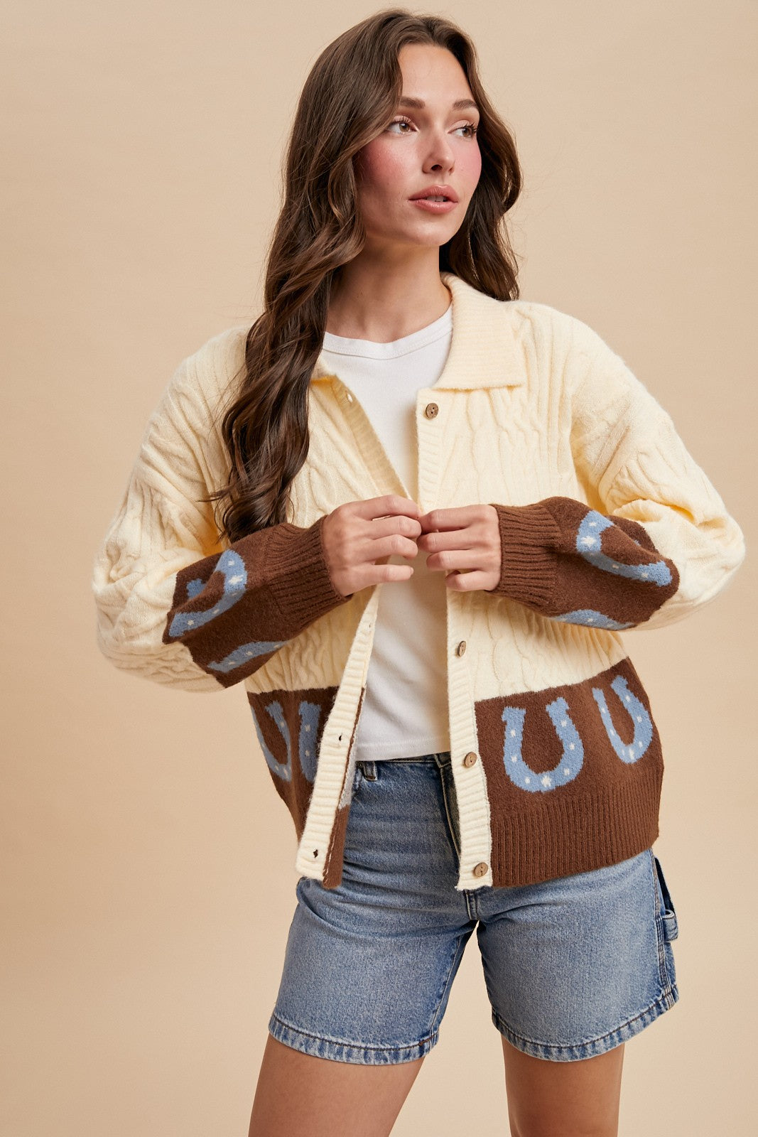 Woman wearing a cream and brown cardigan with blue horseshoes on a beige background