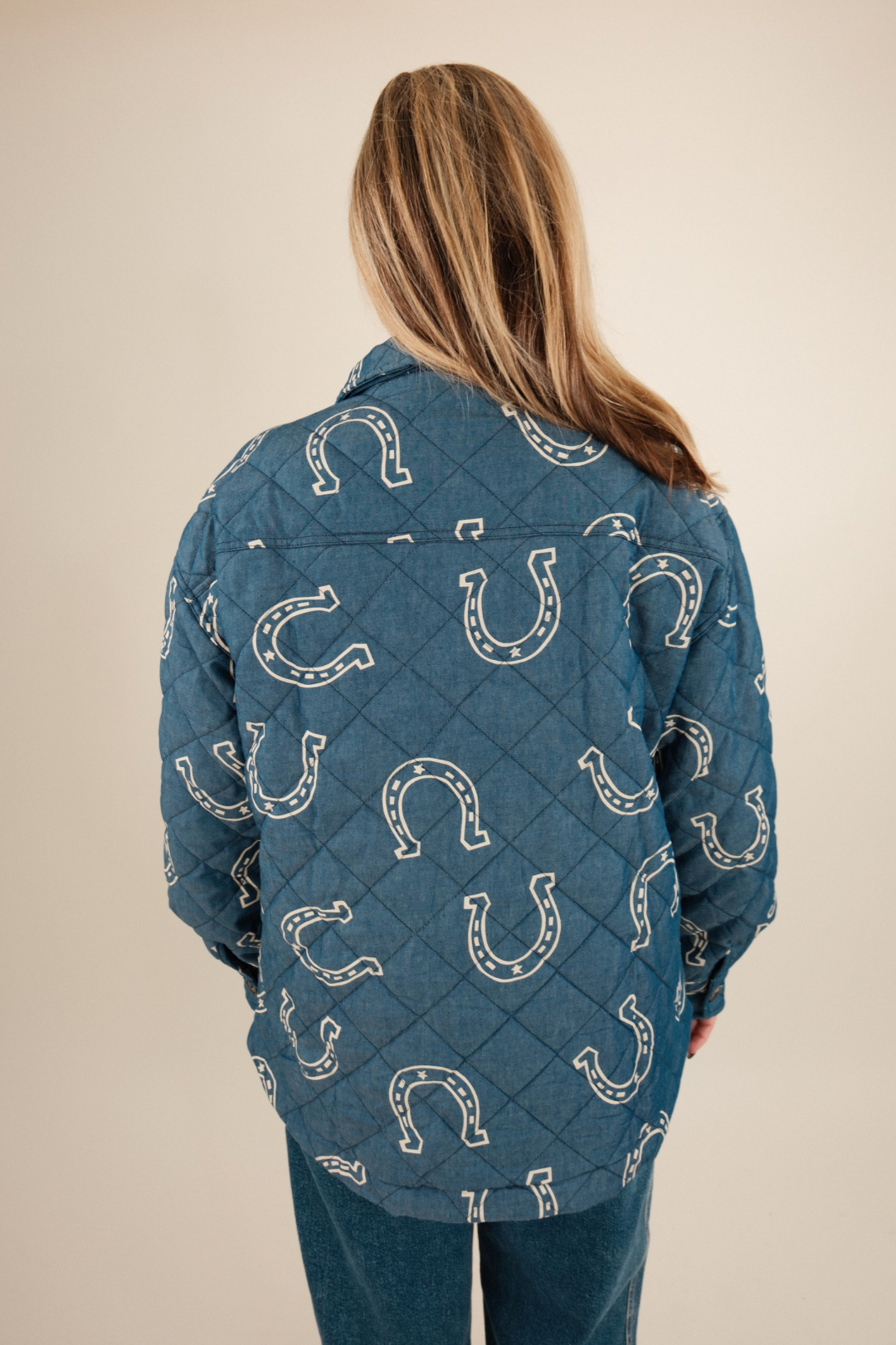 Back view of Lucky Stitch Quilted Denim Jacket featuring allover cream horseshoe print on medium wash quilted denim with western flair.