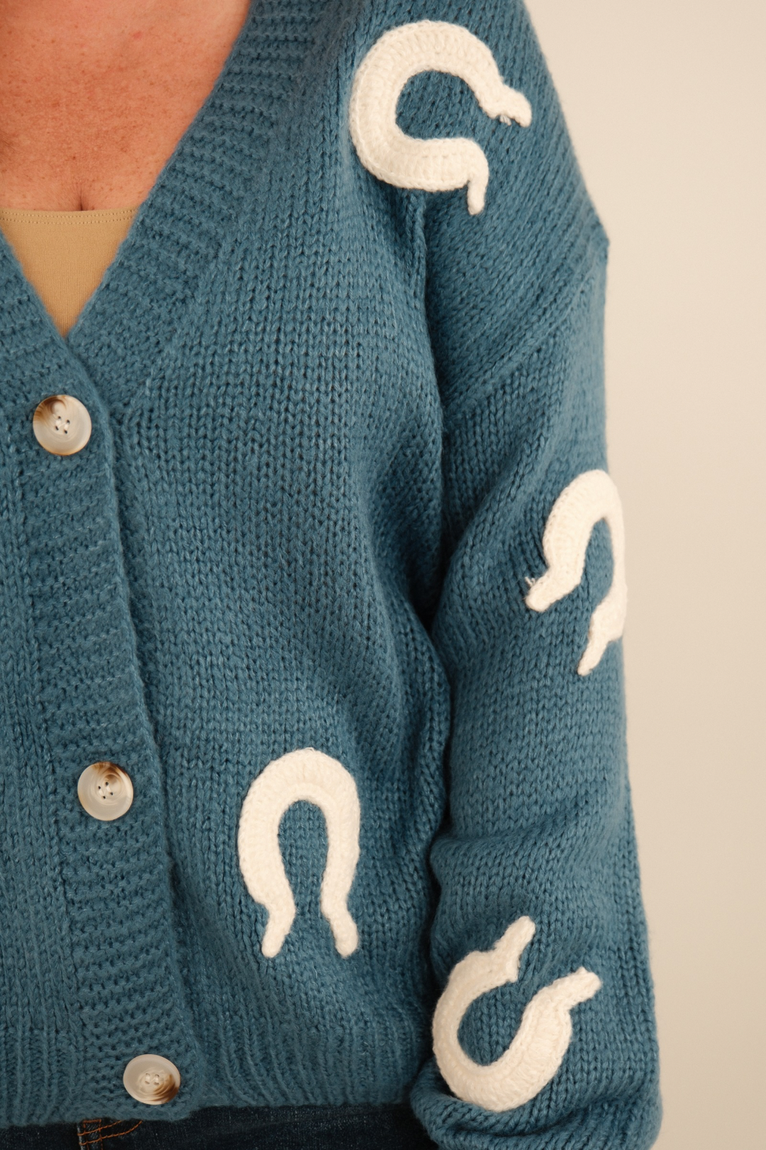 Close-up of Lucky Stitches Cardigan in denim blue highlighting textured knit fabric, cream horseshoe embroidery and button detail