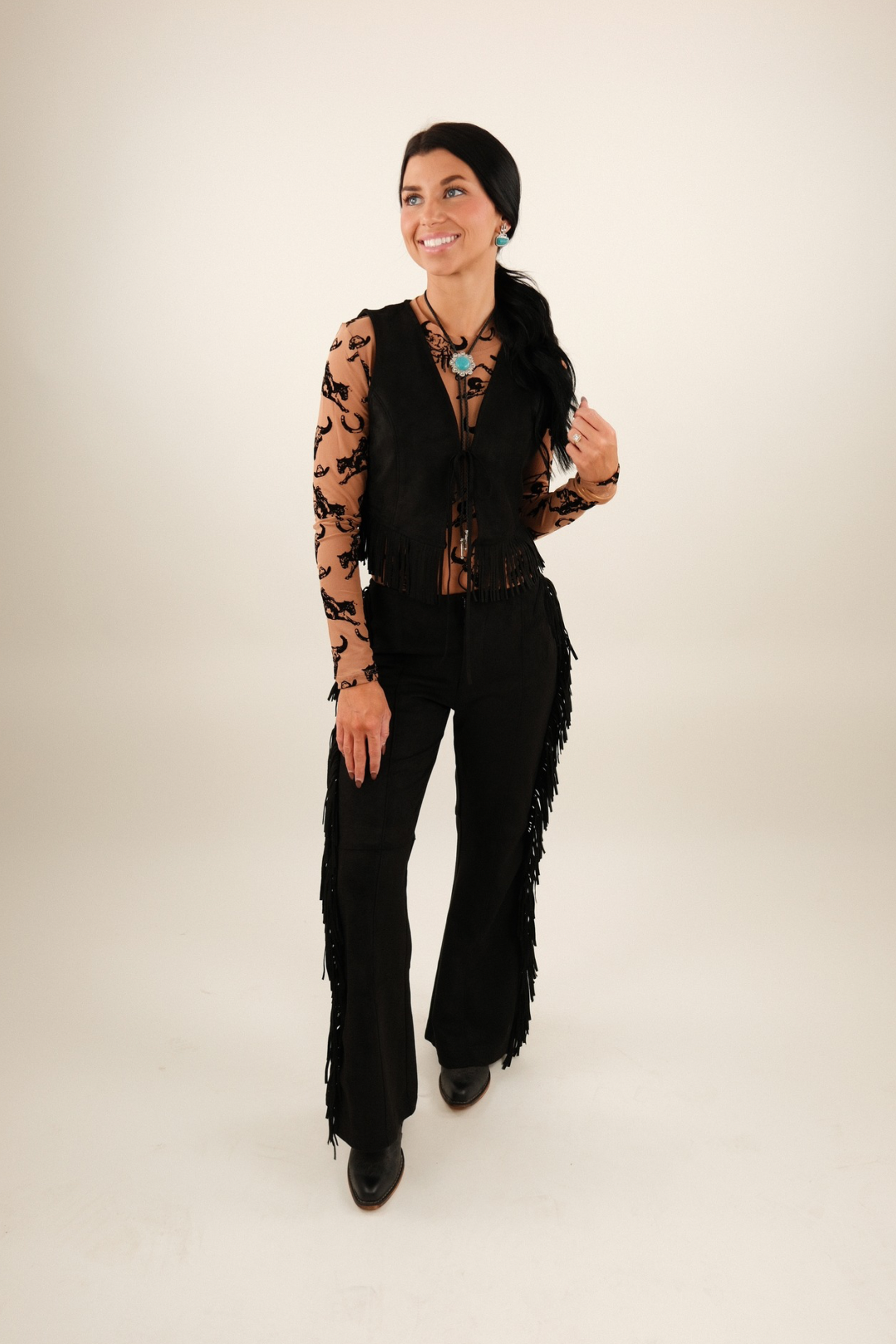 Full body shot of model wearing Midnight Fringe Suede Pants styled with boots, high-rise black suede pants with western fringe detail.