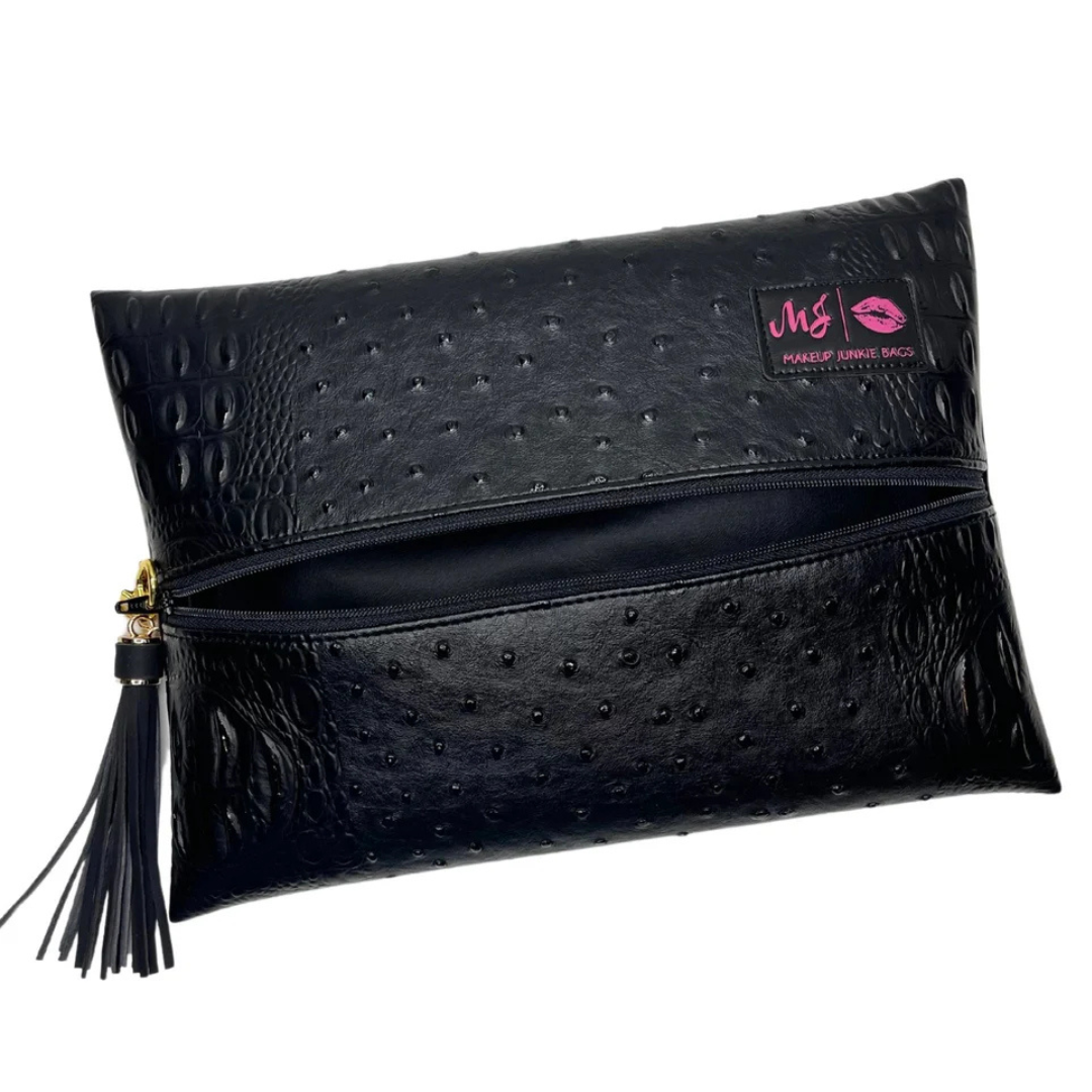 Front view of Obsidian Makeup Junkie bag in jet‑black vegan leather with matte finish, gold zipper and branded tassel detail.