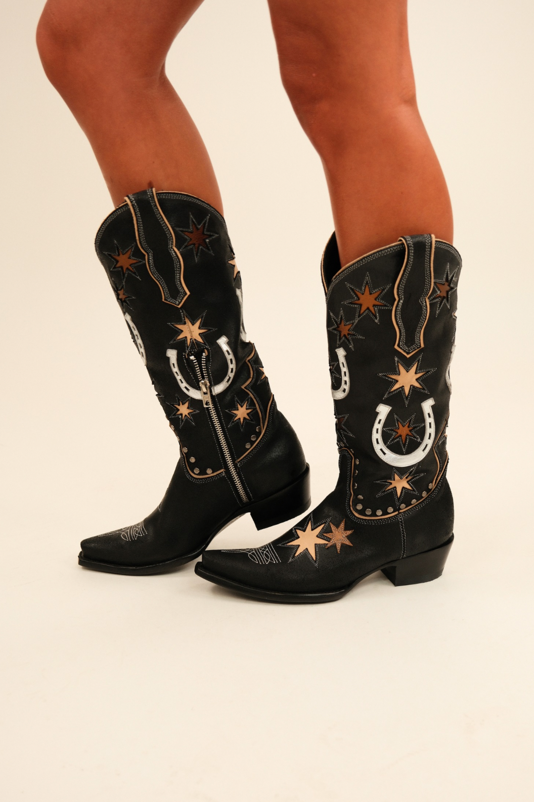 Model wearing black leather Old Gringo Lucky Star boots with bronze stars, silver horseshoes, studs, snip toes, and side zippers.