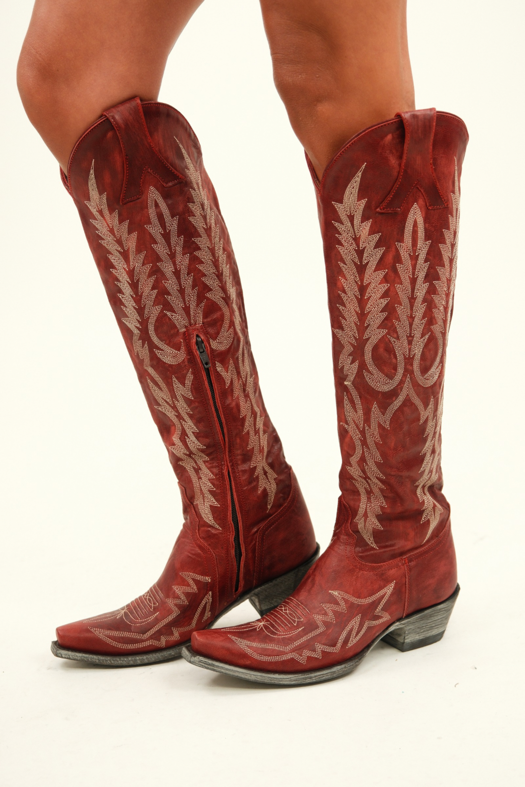 Close‑up of single boot shaft showing intricate ivory zigzag embroidery over rich red leather, inner zipper pull tab and inside seam.