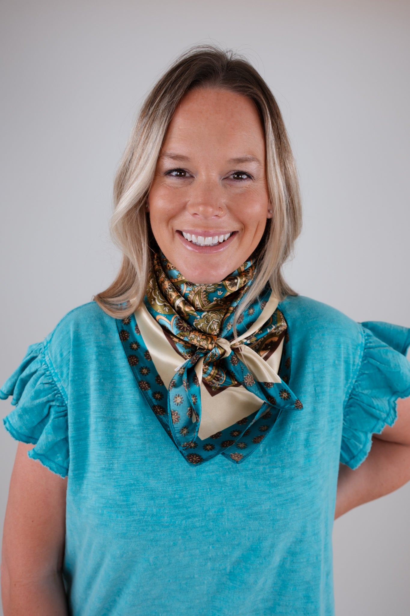 Woman wearing a blue top and patterned scarf against a plain background
