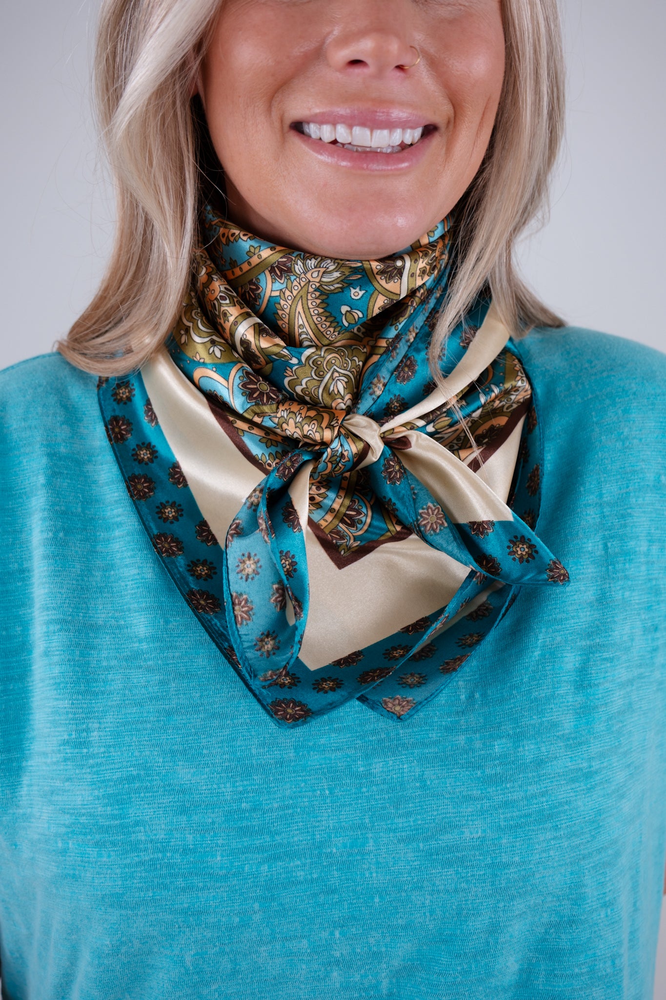 Woman wearing a blue and gold patterned scarf around her neck against a white background