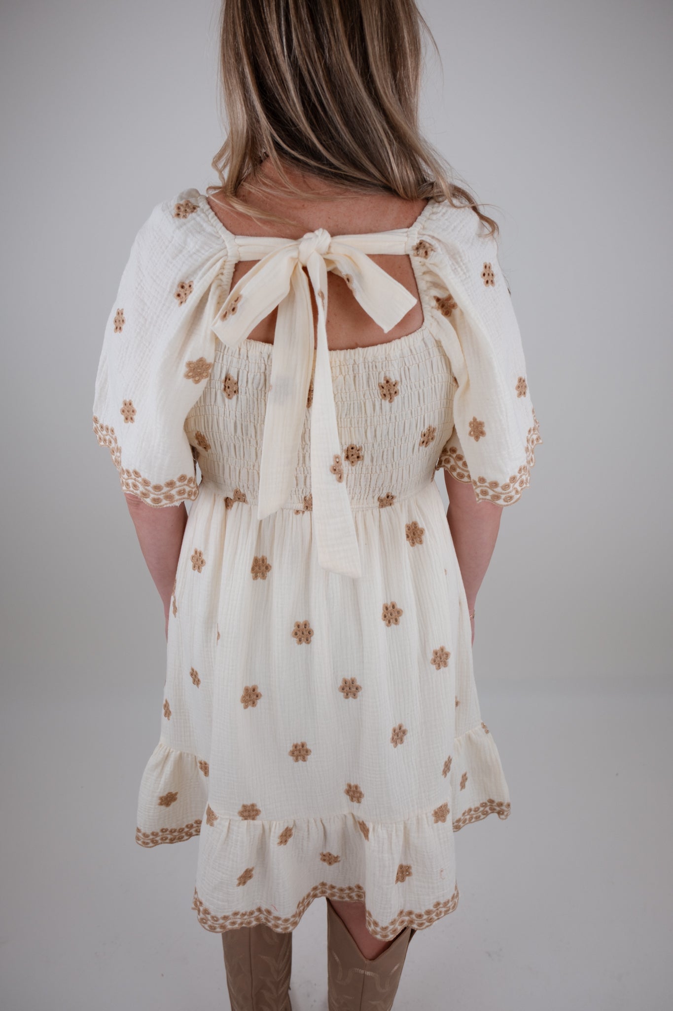 White dress with eyelet floral patterns and open back on a plain background
