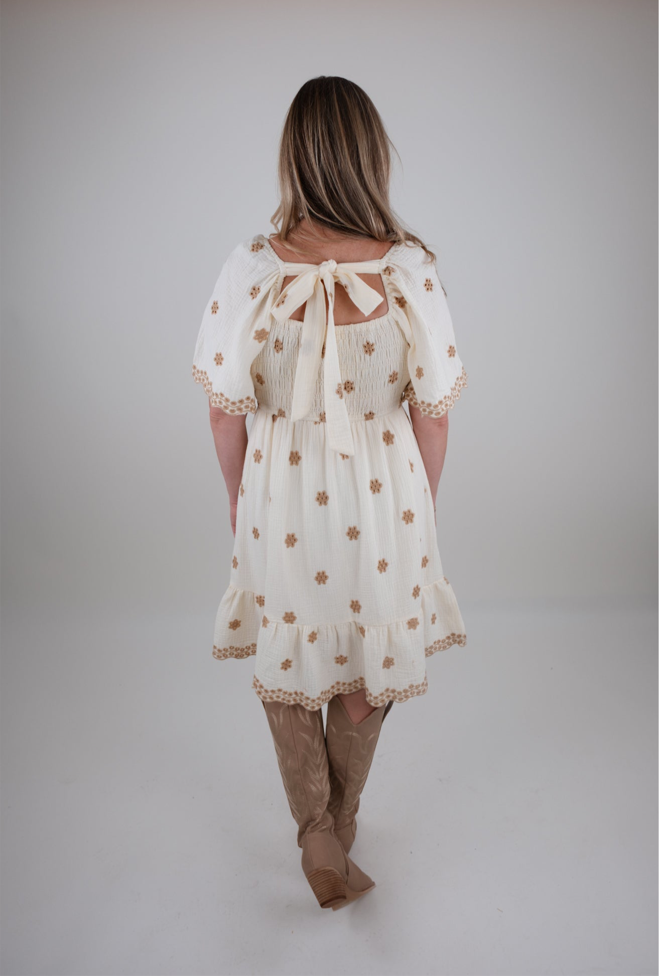 Woman wearing a white dress with eyelet floral patterns on a plain background