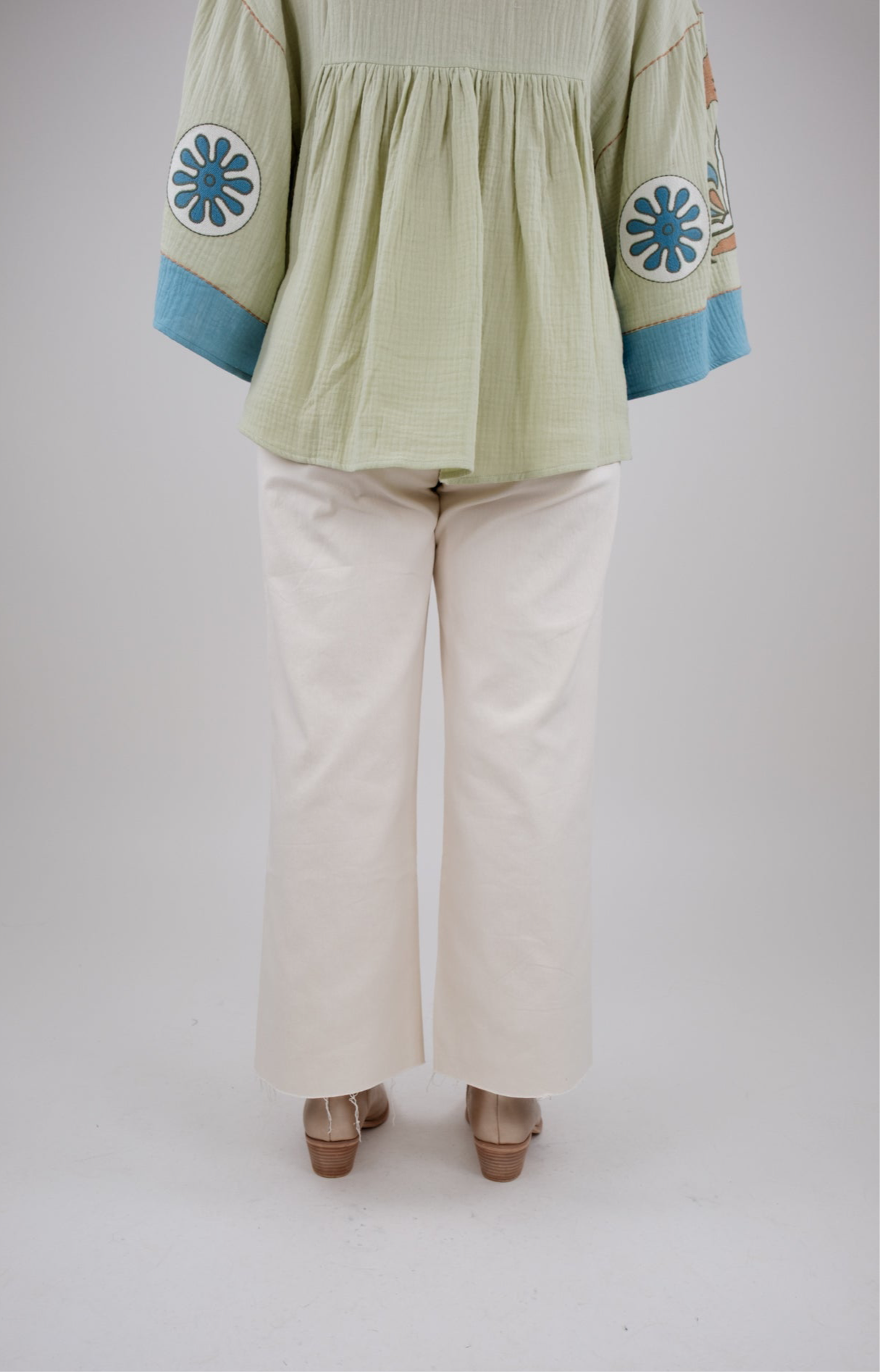 Light green blouse with blue accents and white pants on a plain background