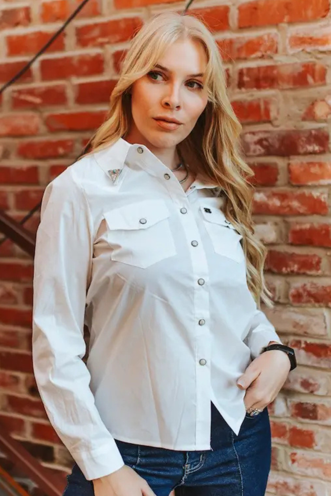 Woman wearing a white button-up shirt against a brick wall