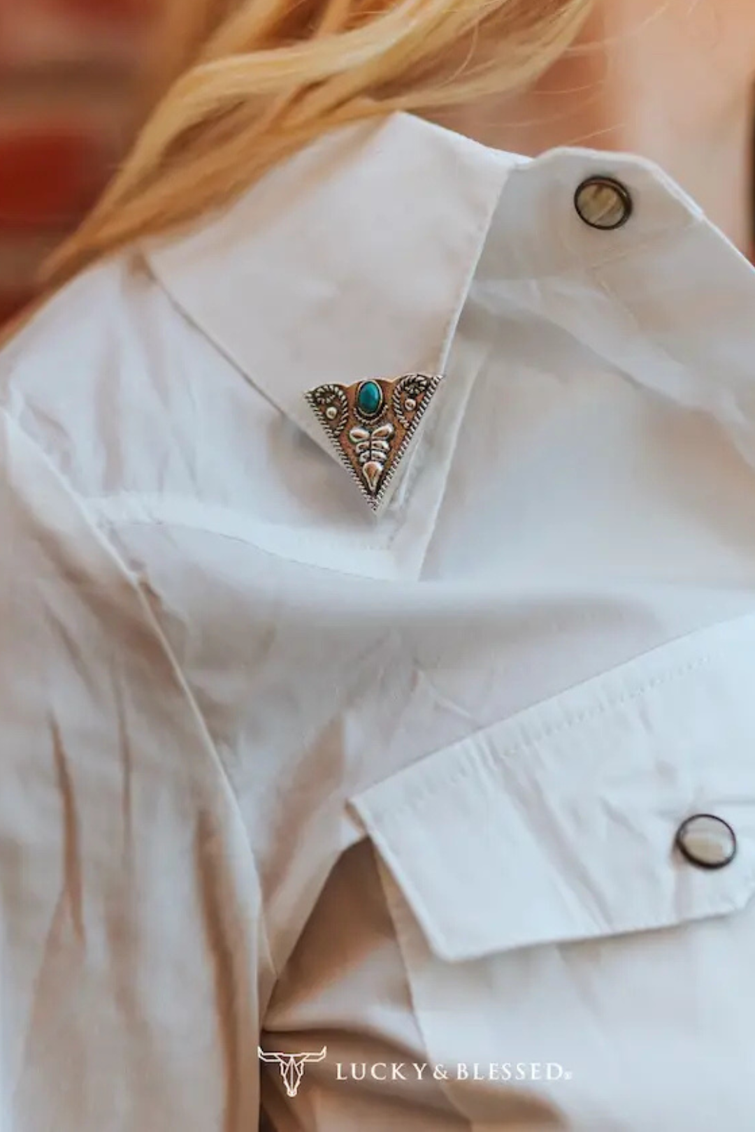 Close-up of a white shirt with a decorative brooch featuring a turquoise stone and silver accents.