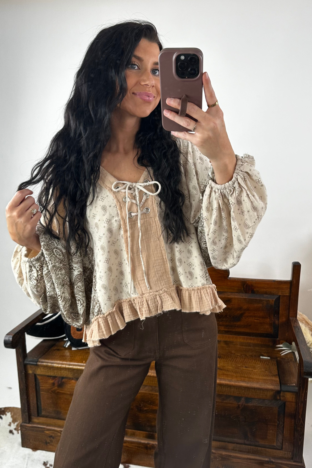 Woman taking a mirror selfie wearing a patterned top and brown pants.