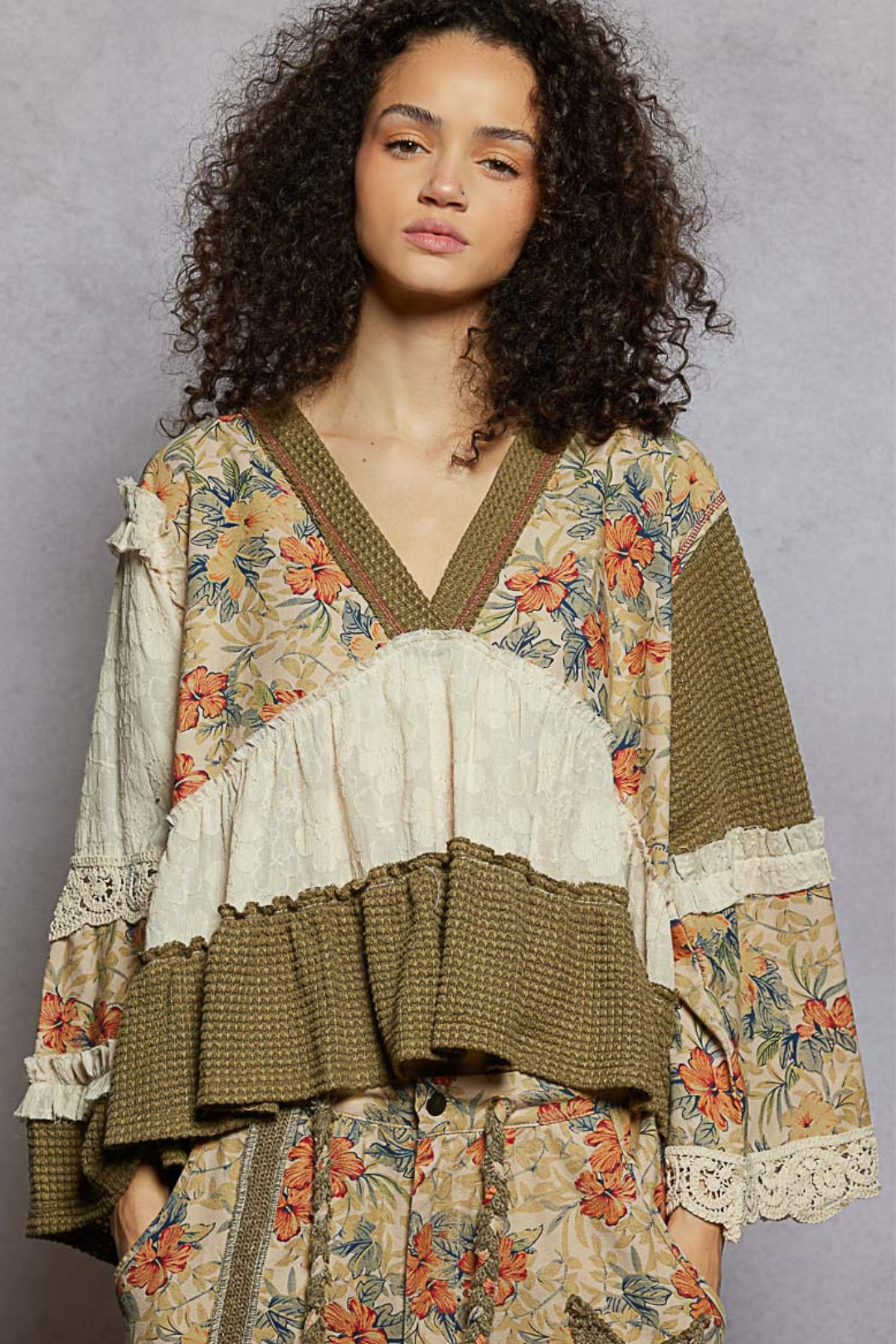 Woman wearing a patchwork floral and ruffled blouse against a gray background