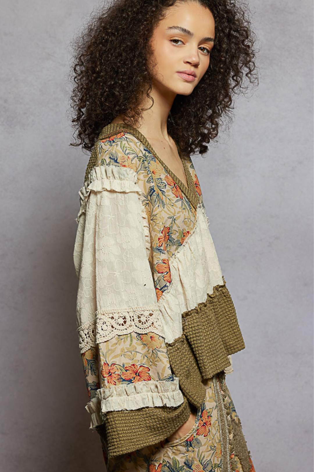Woman wearing a patchwork floral and textured blouse against a gray background
