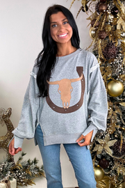 Woman wearing a gray sweatshirt with a longhorn design in front of a decorated Christmas tree.