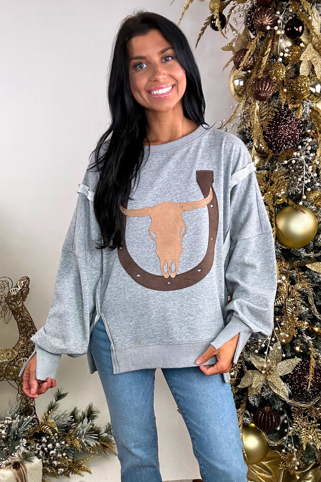 Woman wearing a gray sweatshirt with a longhorn design in front of a decorated Christmas tree.