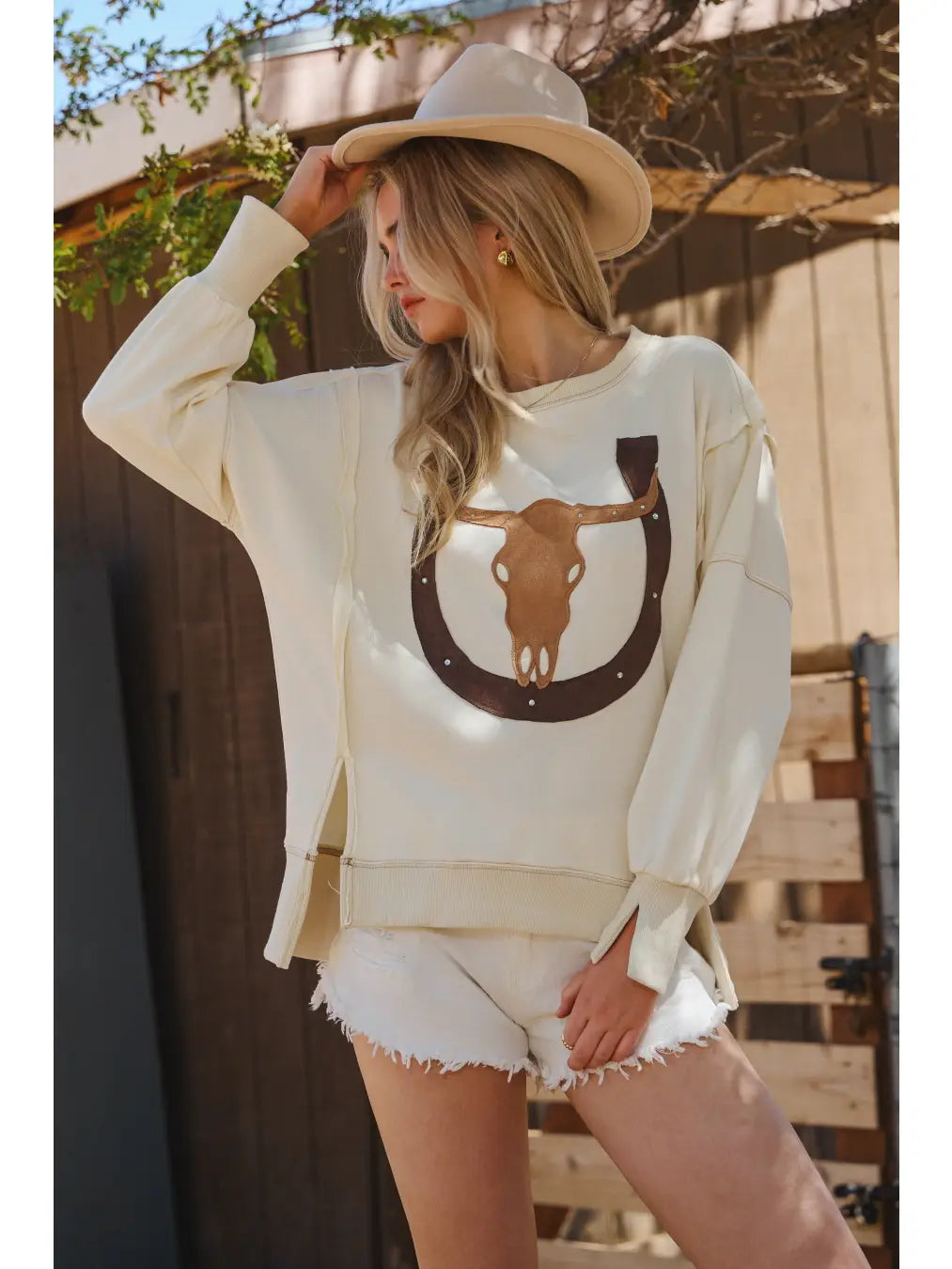 Woman wearing a white sweatshirt with a horse and horseshoe design outdoors.